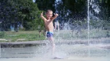 yedi yaşında eğleniyor arasında su jetleri, Çeşme, etrafta çocuk heyecanlı, serpin, iyi eğlenceler, iyi eğlenceler, sıcak yaz gününde. Şehirde yaz. Ağır çekim