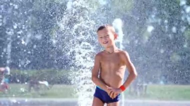 Mutlu çocuk mayo, yedi yıllık su sıçramalarına çeşme arasında eğleniyor. Güneşli yaz günü şehirde. Ağır çekim.