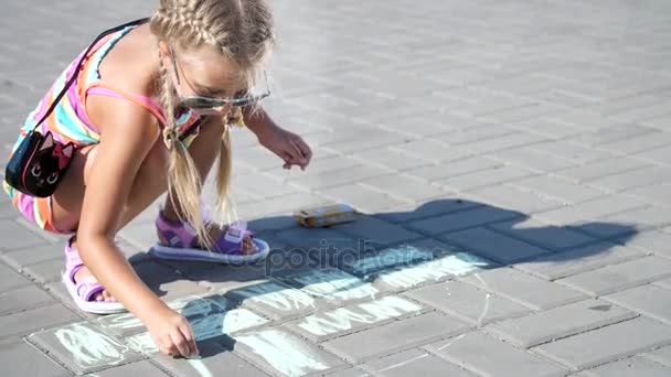 Seorang gadis berkacamata hitam, menggambar dengan krayon berwarna di aspal, ubin jalan. Sebuah hari musim panas . — Stok Video