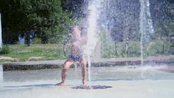 Возбужденный мальчик семи лет, веселящийся между струями воды, в фонтане, бегать вокруг, посыпать, веселиться, веселиться, в жаркий летний день. Лето в городе. Медленное движение — стоковое видео