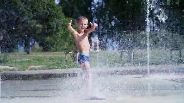 Chico emocionado de siete años divirtiéndose entre chorros de agua, en la fuente, correr, espolvorear, divertirse, divertirse, en un día caluroso de verano. Verano en la ciudad. Movimiento lento — Vídeos de Stock