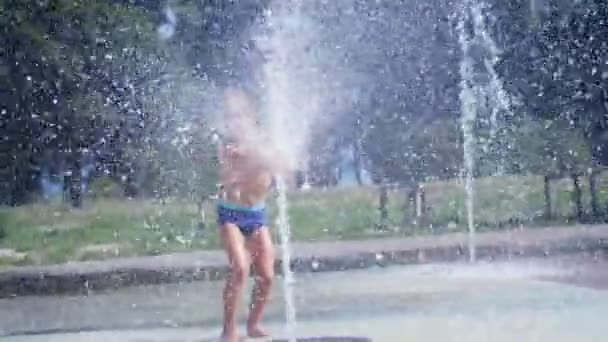 Garoto animado de sete anos se divertindo entre jatos de água, na fonte, corra, polvilhe, divirta-se, divirta-se, em um dia quente de verão. Verão na cidade. Movimento lento — Vídeo de Stock