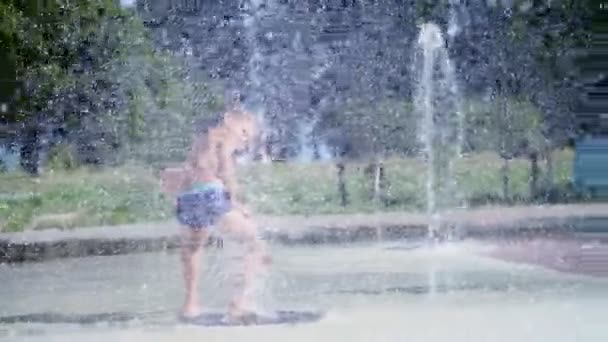 Chico emocionado de siete años divirtiéndose entre chorros de agua, en la fuente, correr, espolvorear, divertirse, divertirse, en un día caluroso de verano. Verano en la ciudad. Movimiento lento — Vídeo de stock