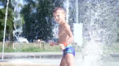 Sevimli çocuk, eğleniyor, yedi yaşında bir çocuk küveti bir çeşme ve oynarken su sıçrama içinde dışarıda, sıcak bir yaz günü. Ağır çekim