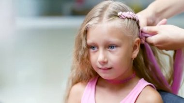 Güzel sarışın kız, yedi yaşında, iki kuyruklu örgülü, Güzellik Salonu, büyük bir ayna önünde bir kuaför salonu saç pembe kilitleri ile bir saç modeli yapmak. küçük bir prenses