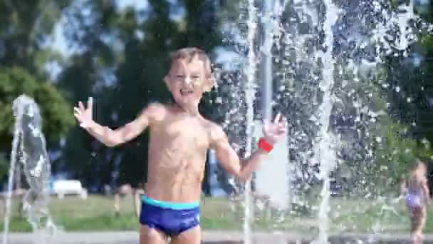 Симпатичный ребенок, семилетний мальчик, веселится, купается в фонтане и играет в брызги воды на улице, в жаркий летний день. Медленное движение — стоковое видео