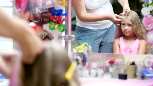 美丽的金发女孩，七岁，编织两个扎着马尾辫、 做发型与粉红色头发锁，在一家美容院，美发沙龙，在大镜子前。小公主 — 图库视频影像