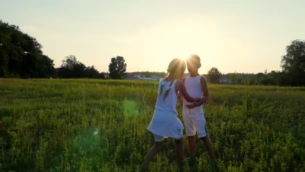 Silhouetten, Figuren von Kindern, Jungen und Mädchen, die sich vor dem Hintergrund der Sonne umarmen, bei Sonnenuntergang im Sommer. glückliche Familie. Zeitlupe — Stockvideo
