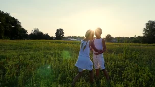 Silhuetas, figuras de crianças, menino e menina abraçando no fundo do sol, ao pôr do sol no verão. Família feliz. Movimento lento — Vídeo de Stock