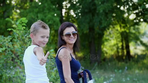 Uma mulher e um menino estão andando pelo campo, o filho está montando um pônei, a mãe está segurando um pônei por um freio. Férias alegres e felizes em família. Ao ar livre, no verão, perto da floresta — Vídeo de Stock