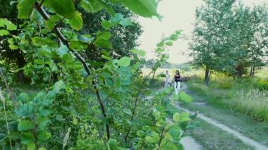 Bir kadın ve bir çocuk etrafında alanı yürüyor, oğlum bir midilli sürme, anne midilli a at başlığı için bekletme. Neşeli, mutlu aile tatili. Forest yakınındaki yaz aylarında açık havada