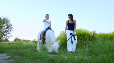 Bir kadın ve bir çocuk etrafında alanı yürüyor, oğlum bir midilli sürme, anne midilli a at başlığı için bekletme. Neşeli, mutlu aile tatili. Forest yakınındaki yaz aylarında açık havada