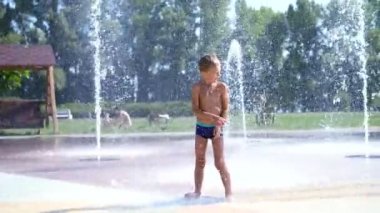 yedi yaşında eğleniyor arasında su jetleri, Çeşme, etrafta çocuk heyecanlı, serpin, iyi eğlenceler, iyi eğlenceler, sıcak yaz gününde. Şehirde yaz. Ağır çekim