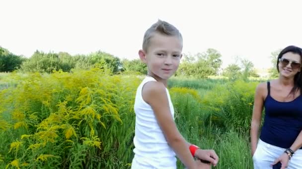 Una mujer y un niño están caminando por el campo, el hijo está montando un pony, la madre está sosteniendo un pony por una brida. Felices y alegres vacaciones en familia. Al aire libre, en verano, cerca del bosque — Vídeos de Stock