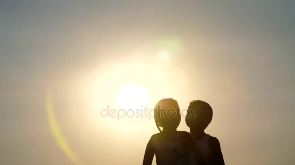 Siluetas, figuras de niños, niños y niñas saltando, divirtiéndose, bailando, abrazándose contra el fondo del sol, al atardecer en verano. Familia feliz. Movimiento lento — Vídeos de Stock