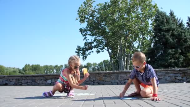 Niños, un niño y una niña en gafas de sol, pintar con lápices de colores en el asfalto, azulejos de la calle. Un caluroso día de verano . — Vídeos de Stock