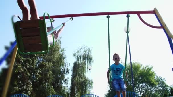 Happy children, a girl and a boy of seven, ride on a swing, on a hot summer day. Slow motion. Cheerful happy childhood, vacation. — Stock Video