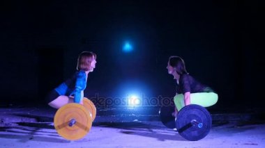 İki atletik kızlar, sporcular, halter yükseltmek, mekik halter ile yap. Geceleri, projektörler, hangarda bir eski terk edilmiş, Bina hafif duman, sis ışığında.