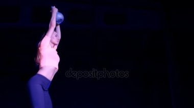 Ağırlıkları ile çeşitli güç egzersizleri yapıyor atletik, güzel genç bir kadın. Geceleri, projektörler, hangarda bir eski terk edilmiş, Bina hafif duman, sis ışığında