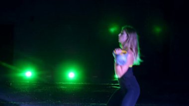 Ağırlıkları ile çeşitli güç egzersizleri yapıyor atletik, güzel genç bir kadın. Geceleri, projektörler, hangarda bir eski terk edilmiş, Bina hafif duman, sis ışığında