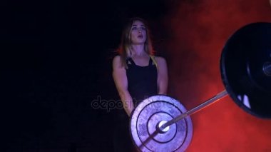 Çift ile çeşitli güç egzersizleri yapıyor iki atletik kızlar halter, ağız kavgası, gece, terk edilmiş eski bir hangarda hafif duman, siste çok renkli projektörler ışığında,