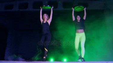 İki atletik, güzel, gece, terk edilmiş eski bir hangarda çok renkli projektörler ışığında hafif duman, sis ağır plakalı güç egzersizleri yapıyor kadın,