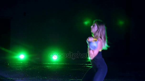 Atletisch, mooie, jonge vrouw, doen van verschillende sterkte-oefeningen met gewichten. 'S nachts, in het licht van zoeklichten, in lichte rook, mist, in een oude verlaten hangar, het gebouw — Stockvideo