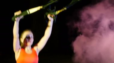 atletik, seksi bir kadın fitness trx sistemi, Trx askı kayışları ile çalışmaları gerçekleştirir. Gece, çok renkli projektörler, ışığında hafif duman, sis içinde binayı terk