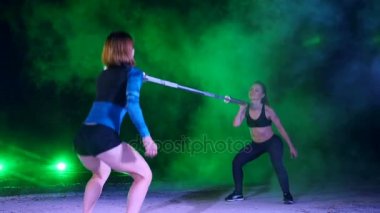 Çift ile çeşitli güç egzersizleri yapıyor iki atletik kızlar halter, ağız kavgası, gece, terk edilmiş eski bir hangarda çok renkli projektörler ışığında hafif duman, sis,