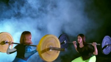 İki atletik kızlar, sporcular, halter yükseltmek, mekik halter ile yap. Geceleri, projektörler, hangarda bir eski terk edilmiş, Bina hafif duman, sis ışığında.