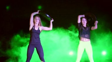 İki atletik, güzel, gece, terk edilmiş eski bir hangarda çok renkli projektörler ışığında hafif duman, sis ağır plakalı güç egzersizleri yapıyor kadın,