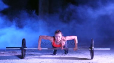 atletik kız itme yapıyor bir halter ile gece, hafif duman, sis, bir eski terk edilmiş hangarda çok renkli projektörler ışığında ups bina