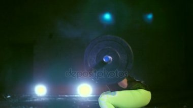 Yan görünümü. atletik kadın, halter yükseltir, halter ile mekik yok. Geceleri hafif duman, sis, çok renkli projektörler ışığında içinde binayı terk edilmiş