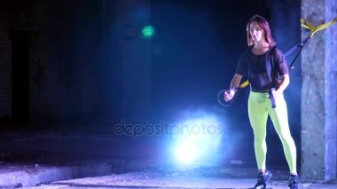 atletik, seksi bir kadın fitness trx sistemi, Trx askı kayışları ile çalışmaları gerçekleştirir. Gece, çok renkli projektörler, ışığında hafif duman, sis içinde binayı terk