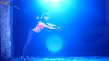 atletik, seksi bir kadın fitness trx sistemi, Trx askı kayışları ile çalışmaları gerçekleştirir. Gece, çok renkli projektörler, ışığında hafif duman, sis içinde binayı terk