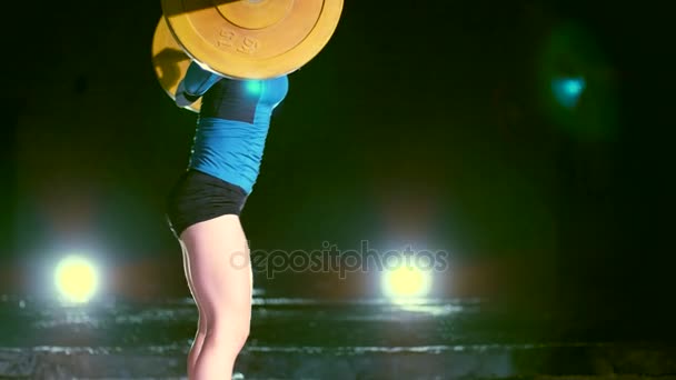 Zijaanzicht. sportieve vrouw, verhoogt de halter, sit-ups met de barbell doet. 'S nachts, in het licht van veelkleurige zoeklichten, in lichte rook, mist, verlaten in oude gebouw — Stockvideo