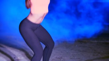 Ağırlıkları ile çeşitli güç egzersizleri yapıyor atletik, güzel genç bir kadın. Geceleri hafif duman, sis, çok renkli projektörler ışığında içinde binayı terk edilmiş