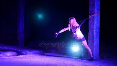 atletik, seksi bir kadın fitness trx sistemi, Trx askı kayışları ile çalışmaları gerçekleştirir. Gece, çok renkli projektörler, ışığında hafif duman, sis içinde binayı terk