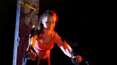 atletik, seksi bir kadın fitness trx sistemi, Trx askı kayışları ile çalışmaları gerçekleştirir. Gece, çok renkli projektörler, ışığında hafif duman, sis içinde binayı terk