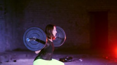 atletik genç kadın, halter yükseltir, mekik ile halter, onun sert onun için yapar. Geceleri hafif duman, sis, çok renkli projektörler ışığında içinde binayı terk edilmiş