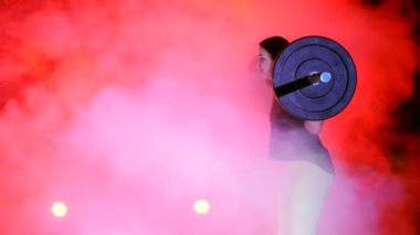 atletik genç kadın, halter yükseltir, mekik ile halter, onun sert onun için yapar. Geceleri hafif duman, sis, çok renkli projektörler ışığında içinde binayı terk edilmiş