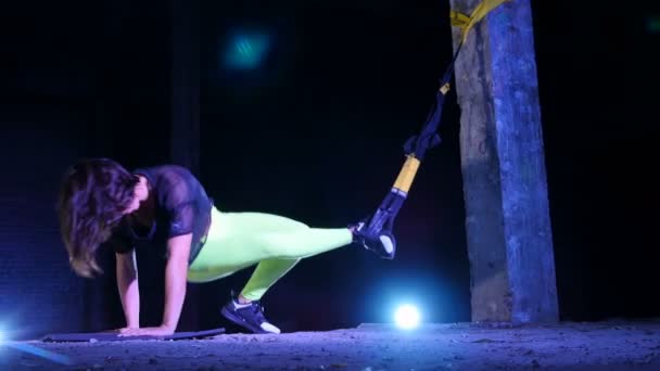 Sportowe, sexy kobieta wykonuje ćwiczenia fitness trx system, taśmy do zawieszania Trx. W nocy, w lekki dym, mgła, w świetle wielobarwny reflektorzy w opuszczonych budynków — Wideo stockowe