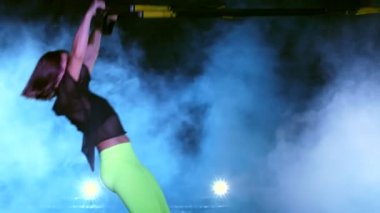 atletik, seksi bir kadın fitness trx sistemi, Trx askı kayışları ile çalışmaları gerçekleştirir. Gece, çok renkli projektörler, ışığında hafif duman, sis içinde binayı terk