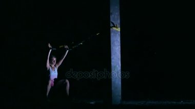 atletik, seksi bir kadın fitness trx sistemi, Trx askı kayışları ile çalışmaları gerçekleştirir. Gece, çok renkli projektörler, ışığında hafif duman, sis içinde binayı terk