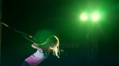 atletik, seksi bir kadın fitness trx sistemi, Trx askı kayışları ile çalışmaları gerçekleştirir. Gece, çok renkli projektörler, ışığında hafif duman, sis içinde binayı terk