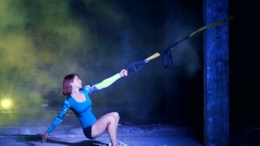 atletik, seksi bir kadın fitness trx sistemi, Trx askı kayışları ile çalışmaları gerçekleştirir. Gece, çok renkli projektörler, ışığında hafif duman, sis içinde binayı terk