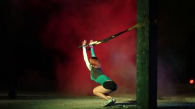 atletik, seksi bir kadın fitness trx sistemi, Trx askı kayışları ile çalışmaları gerçekleştirir. Gece, çok renkli projektörler, ışığında hafif duman, sis içinde binayı terk
