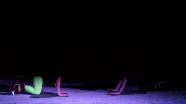 Deux femmes athlétiques, faisant des exercices de fitness avec pondération sur les jambes, La nuit, dans un brouillard léger, à la lumière de projecteurs multicolores et d'un stobascope, dans un vieux hangar abandonné , — Video