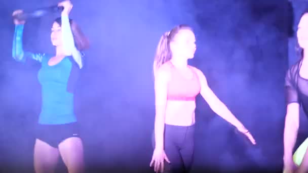 Атлетичные сексуальные женщины, занимающиеся фитнес-упражнениями с тяжестью, ночью, в легком дыму, тумане, в свете соскопа и разноцветных прожекторов, в старом заброшенном здании — стоковое видео