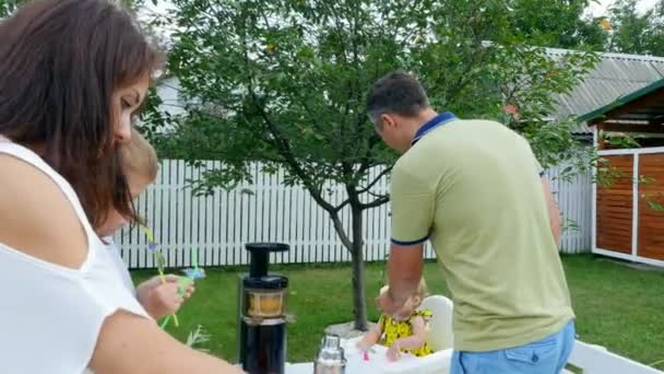 Verano, en el jardín, la familia pone la mesa, la madre y el hijo hacen un ramo de flores, el padre alimenta a su hija con una manzana . — Vídeo de stock